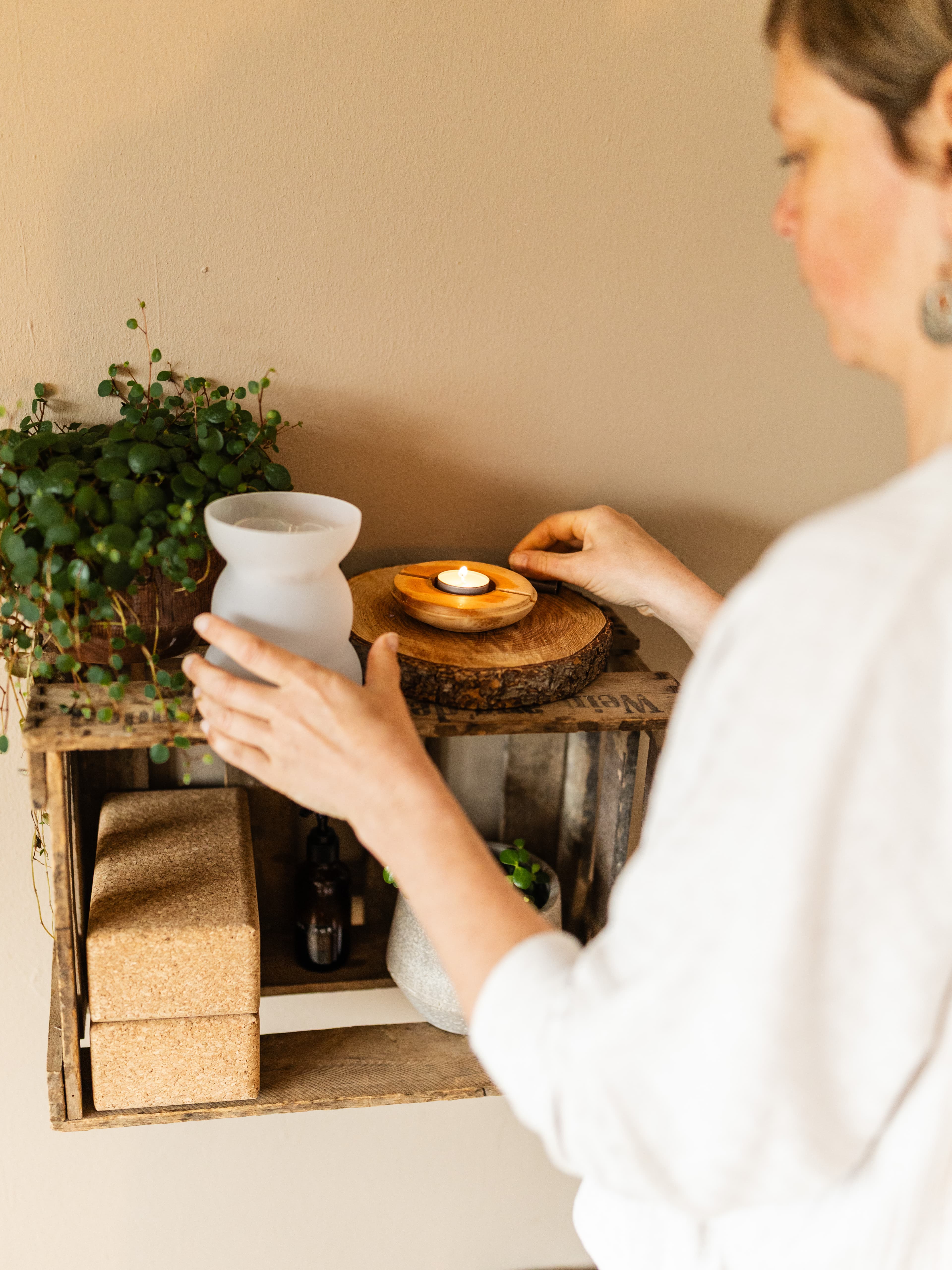 Frau arrangiert Kerze und Yogazubehör auf Holzregal – Gruppenangebote Yoga und Atemarbeit Freiburg